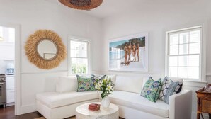 Un salon moderne avec un canapé blanc, une table basse ronde et un grand miroir. Un tableau encadré est accroché au mur et un panier en osier est suspendu au plafond.