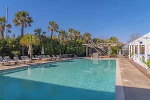 A clear swimming pool with lounge chairs and a covered area, surrounded by palm trees and a building with a white facade. - Blue Cottage | Casa Zoë – Your Charleston Escape (Charleston)