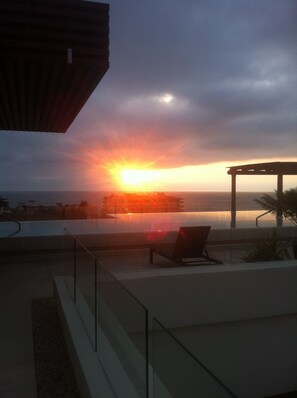 A sunset view from a balcony with a pool, outdoor seating, and a pergola. - Romantic Zone Cozy Studio: Flat Walk to Beach, Restaurants & Nightlife (Puerto Vallarta)