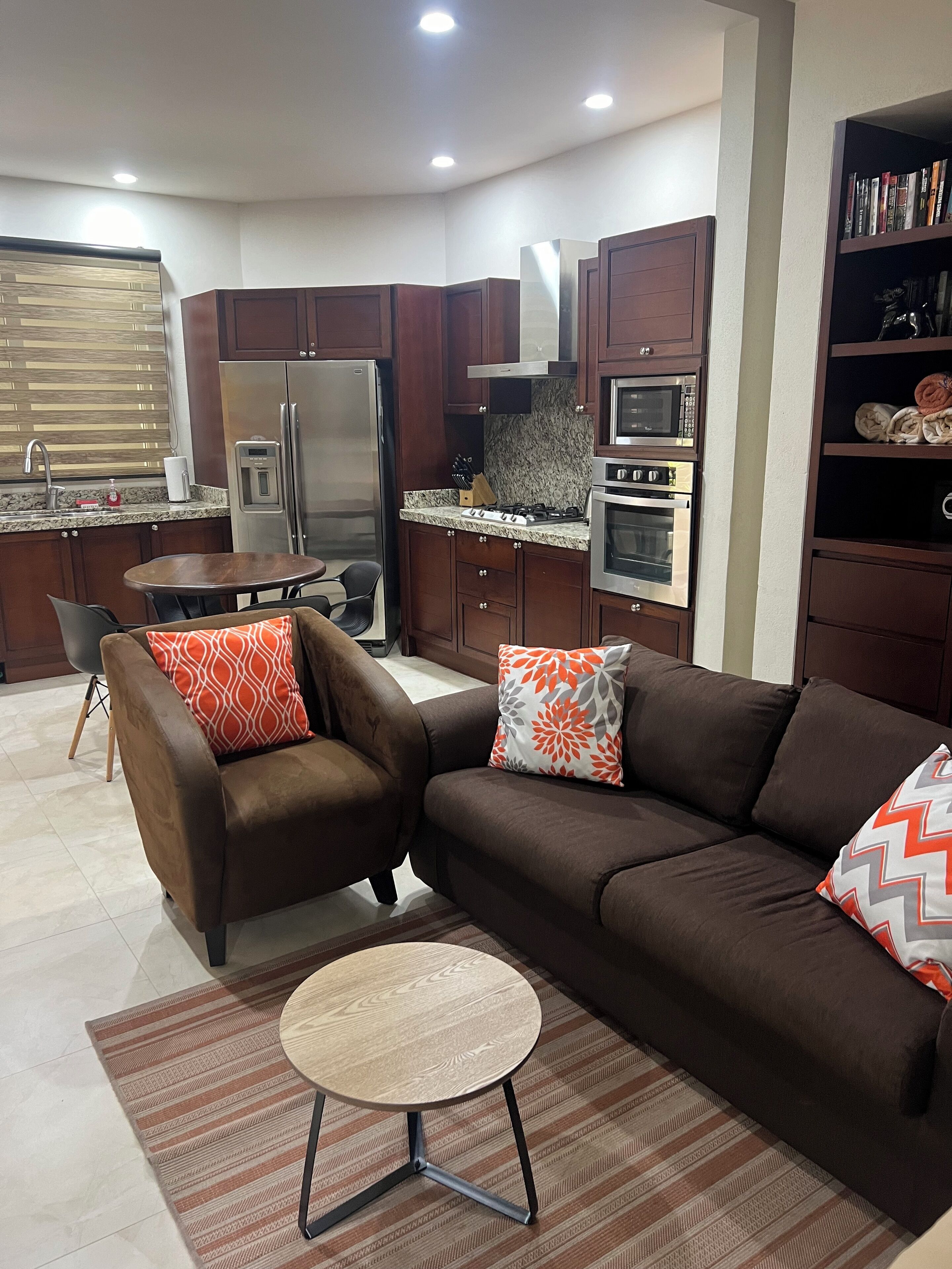 Eine moderne Küche mit Kühlschrank, Herd, Mikrowelle und Backofen. Ein Esstisch mit Stühlen und eine Couch mit Zierkissen sind ebenfalls vorhanden.