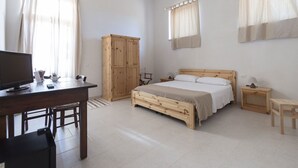 Un dormitorio con cama de madera, escritorio con televisor, armario y mesita de noche con lámpara.