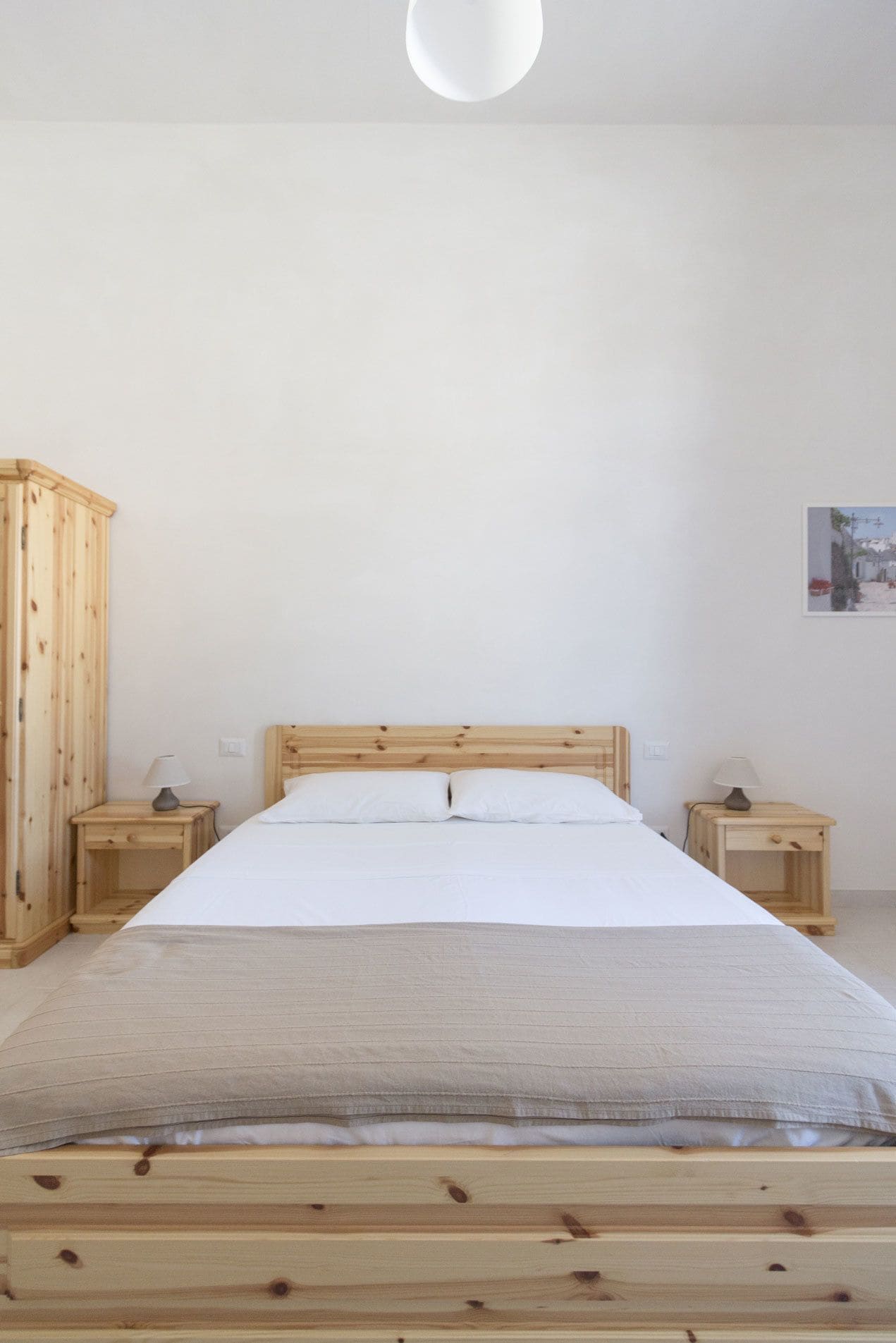 Un dormitorio minimalista con estructura de cama de madera, dos mesitas de noche y una lámpara de pared.