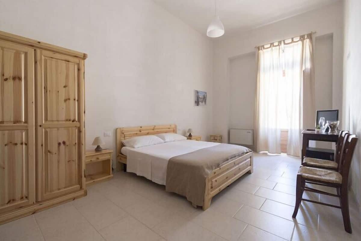 A bedroom with a wooden bed, a nightstand, a desk with a chair, and a wardrobe.