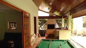 A pool table with balls, a sofa, and a television in a room with a wooden ceiling and a brick fireplace. - Cond Hanga Roa - Bertioga Riviera (Bertioga)