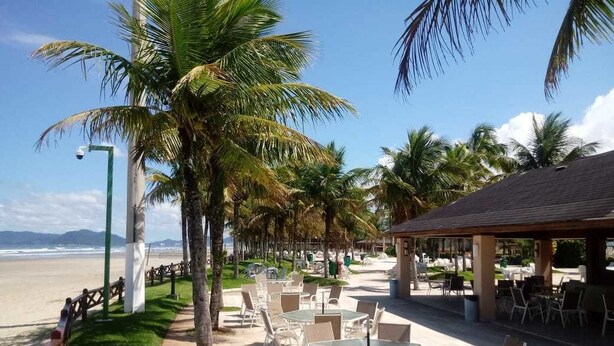 A beachside café with outdoor seating, palm trees, and a view of the ocean. - Cond Hanga Roa - Bertioga Riviera (Bertioga)