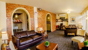 A living room with a brown leather sofa, a coffee table with a green plant, and a fireplace with a brick wall. There is a bookshelf with books and a desk with a computer. - Hotel Carmel (Lima)