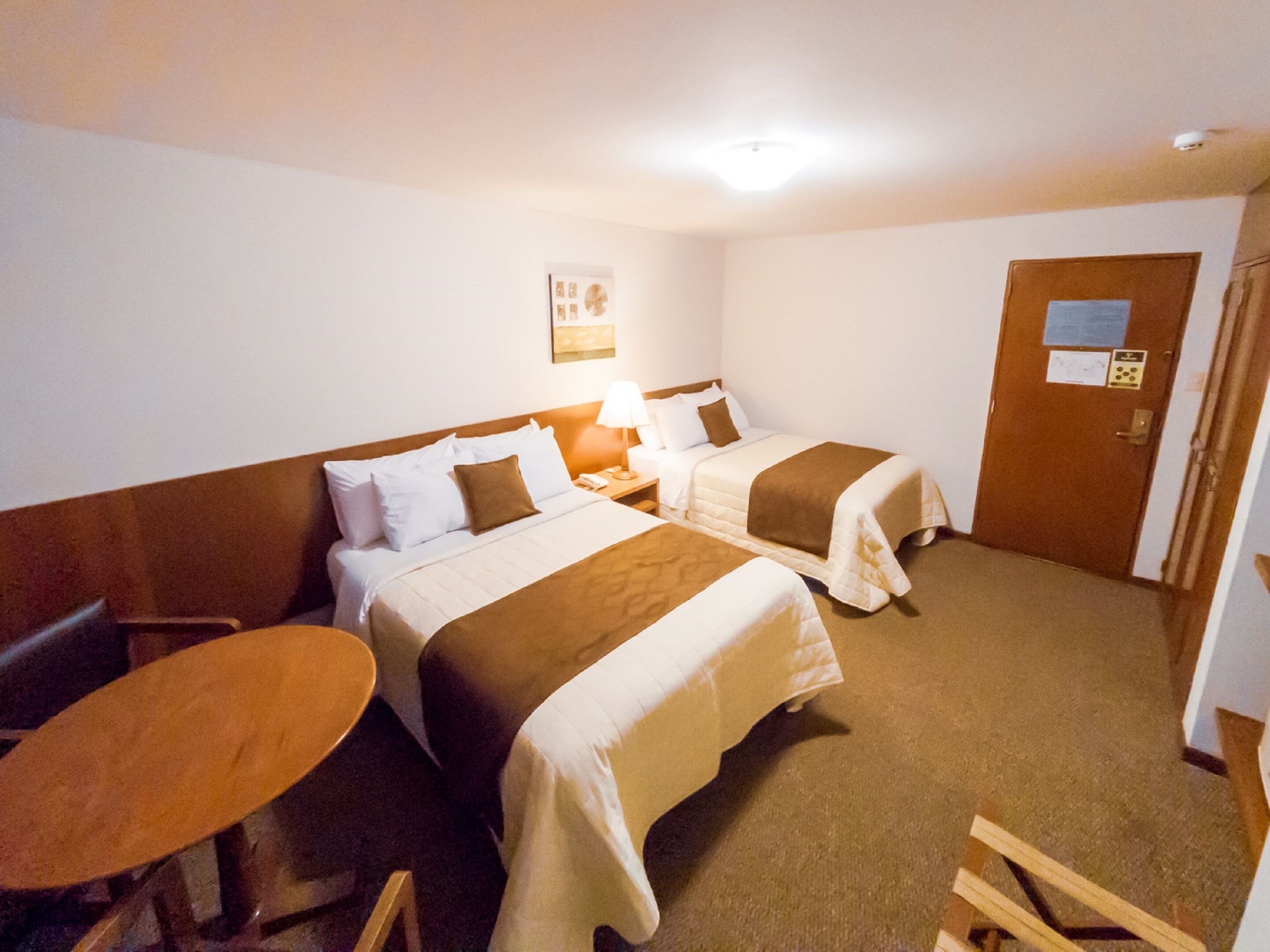 Habitación de hotel con dos camas, una mesita y una puerta.