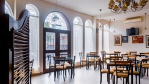 A spacious dining area with multiple tables and chairs, large windows with arched tops, and a chandelier. - Hotel Carmel (Lima)
