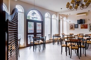 Un vaste espace dédié à la salle à manger, avec de nombreuses tables et chaises, de grandes fenêtres surmontées d’arcs et un lustre.
