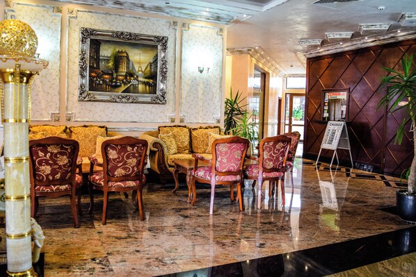 A lobby with a marble floor, a sofa set, a framed painting, and a reception desk. - Karolina (Nessebar)