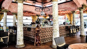 Zona de bar con barra central, varios arreglos de asientos y columnas decorativas.