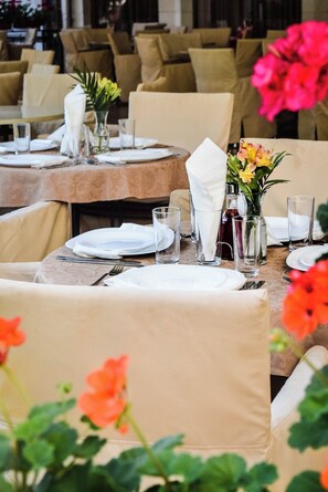 A dining area with round tables, beige chairs, and floral centerpieces. - Karolina (Nessebar)