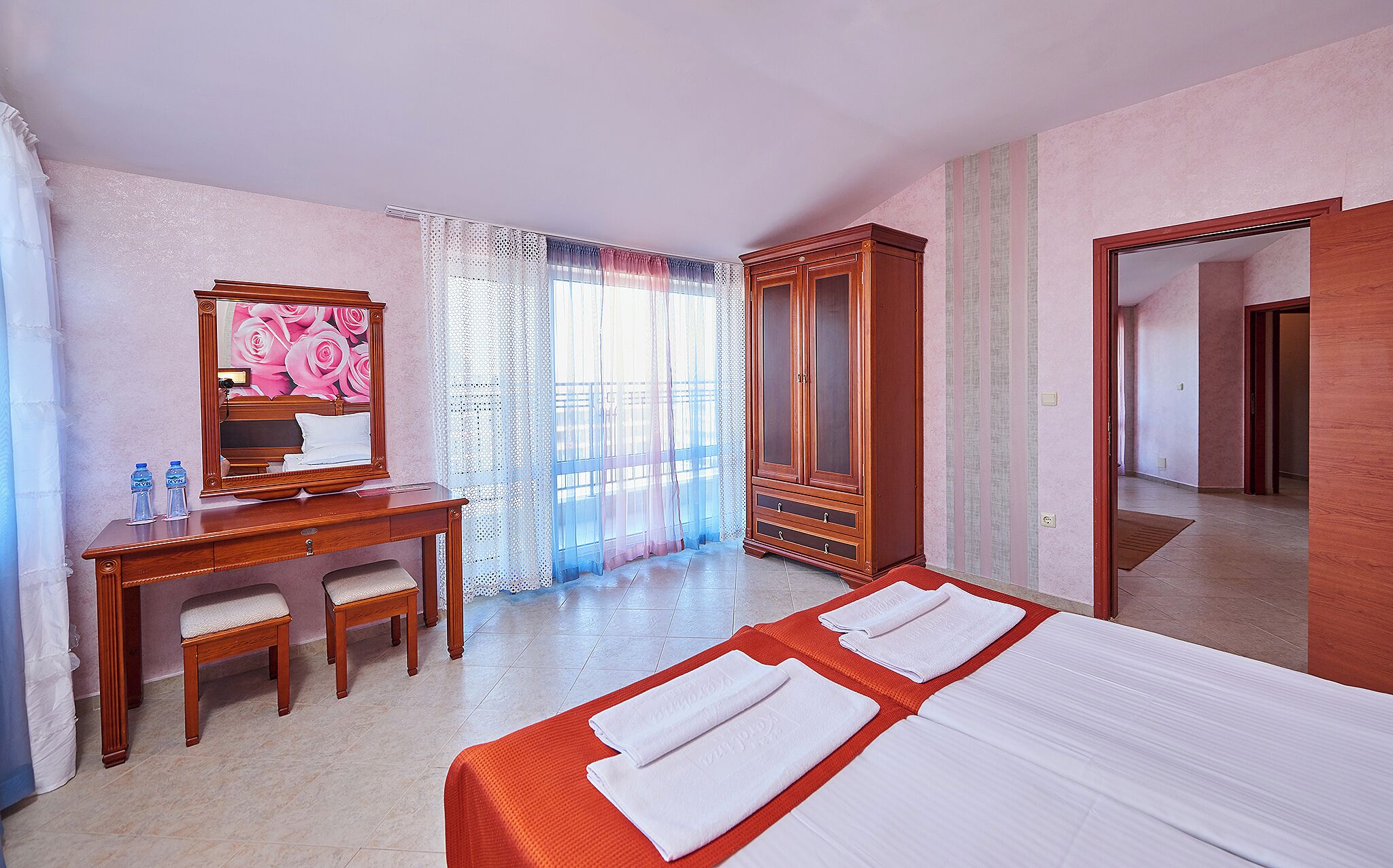 A hotel room with a bed, a desk, a chair, a wardrobe, and a mirror.