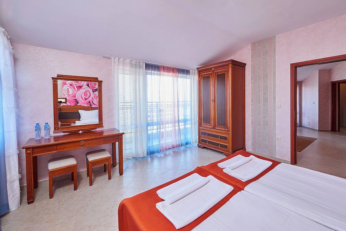 A hotel room with a bed, a desk, a chair, a wardrobe, and a mirror.