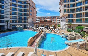 A multi-level hotel with a central pool area featuring a water slide, lounge chairs, and umbrellas.