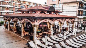 Un área de estar al aire libre con sillones reclinables y sombrillas, un bar y un ambiente junto a la piscina.