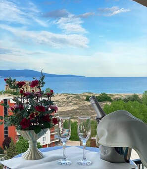 A table with a vase of flowers, two wine glasses, and a bottle opener, overlooking a beach and the sea.