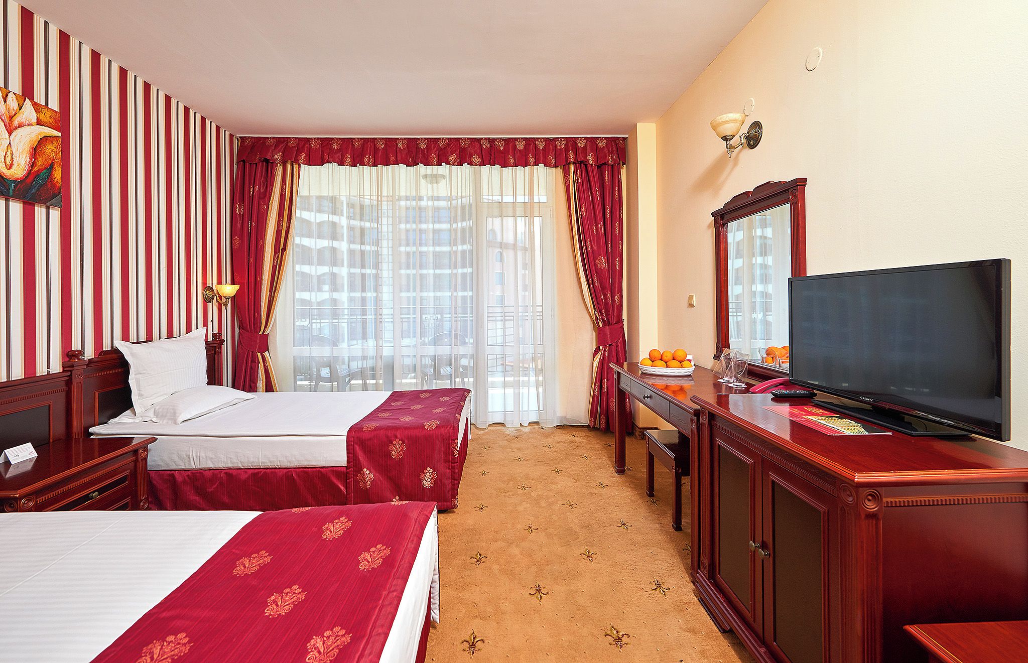 A hotel room with two beds, a TV, a desk with a lamp, and a large window with curtains.