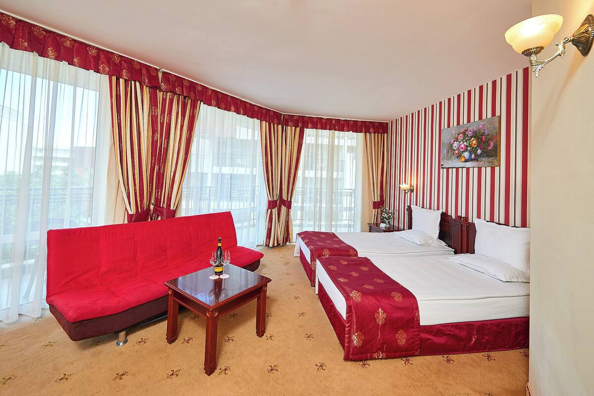 A hotel room with a red sofa, a wooden table, a bed with a red bedspread, and striped wallpaper.