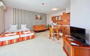 Une chambre d’hôtel comprenant un lit, un canapé, une télévision, une table à manger, des chaises, un coin cuisine et un mur à rayures.