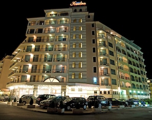 A multi-story hotel with balconies, a parking lot, and a neon sign.