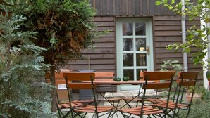 An outdoor patio with a wooden table and chairs, surrounded by greenery. - Stella Apartments (Erfurt)