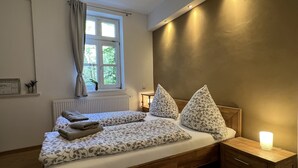A bedroom with a bed, bedside tables, a window with curtains, and a wall-mounted light. - Stella Apartments (Erfurt)