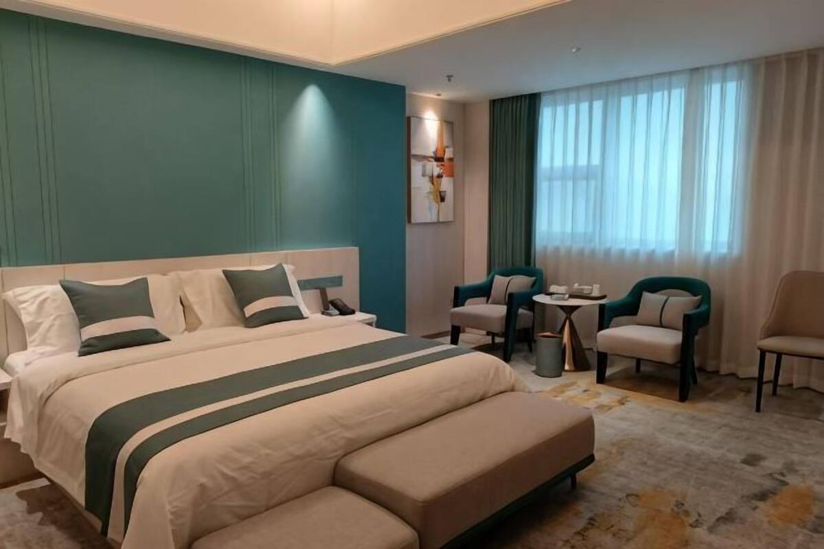 A hotel room with a large bed, a desk, two chairs, and a window with curtains.