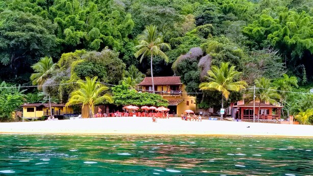 A beachside hotel with outdoor seating, palm trees, and a view of the water. - Pousada Tony Montana (Angra dos Reis)