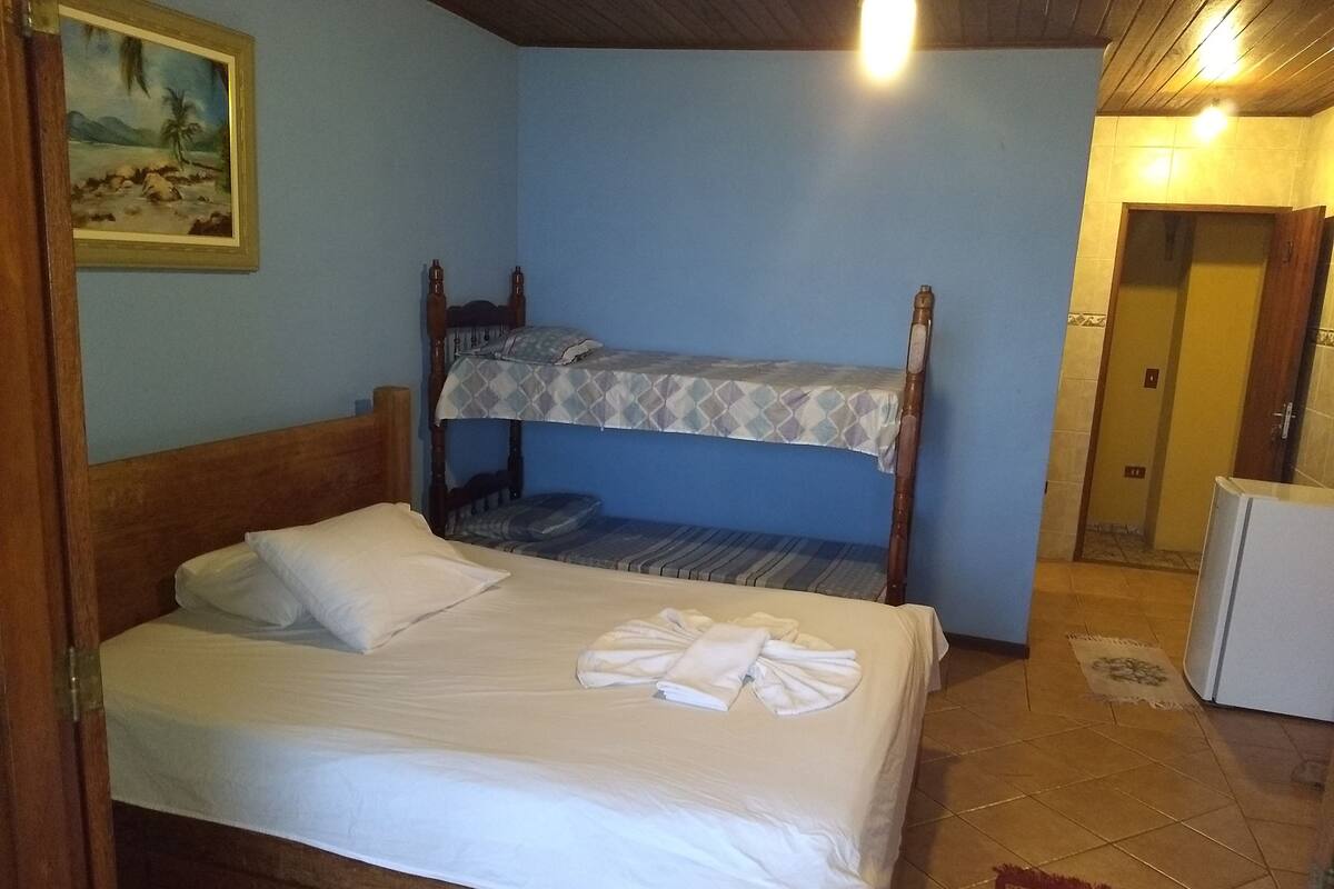 Une chambre avec un lit superposé, un lit simple, un petit réfrigérateur et un tableau accroché au mur.