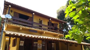 A two-story building with a yellow facade, wooden balconies, and outdoor seating area with tables and chairs. - Pousada Tony Montana (Angra dos Reis)
