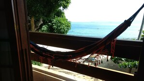 A hammock on a balcony overlooking a beach with a view of the sea and a tree. - Pousada Tony Montana (Angra dos Reis)
