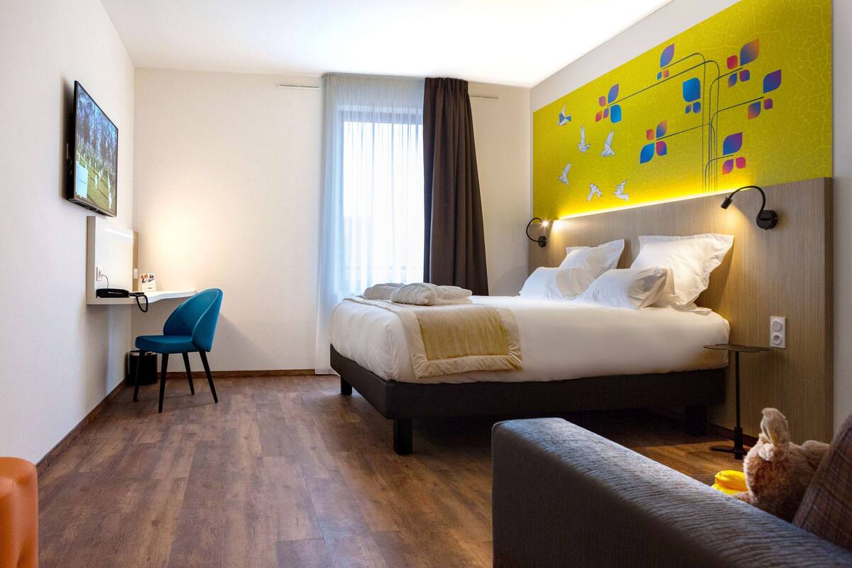 A hotel room with a bed, a desk, a chair, and a couch.