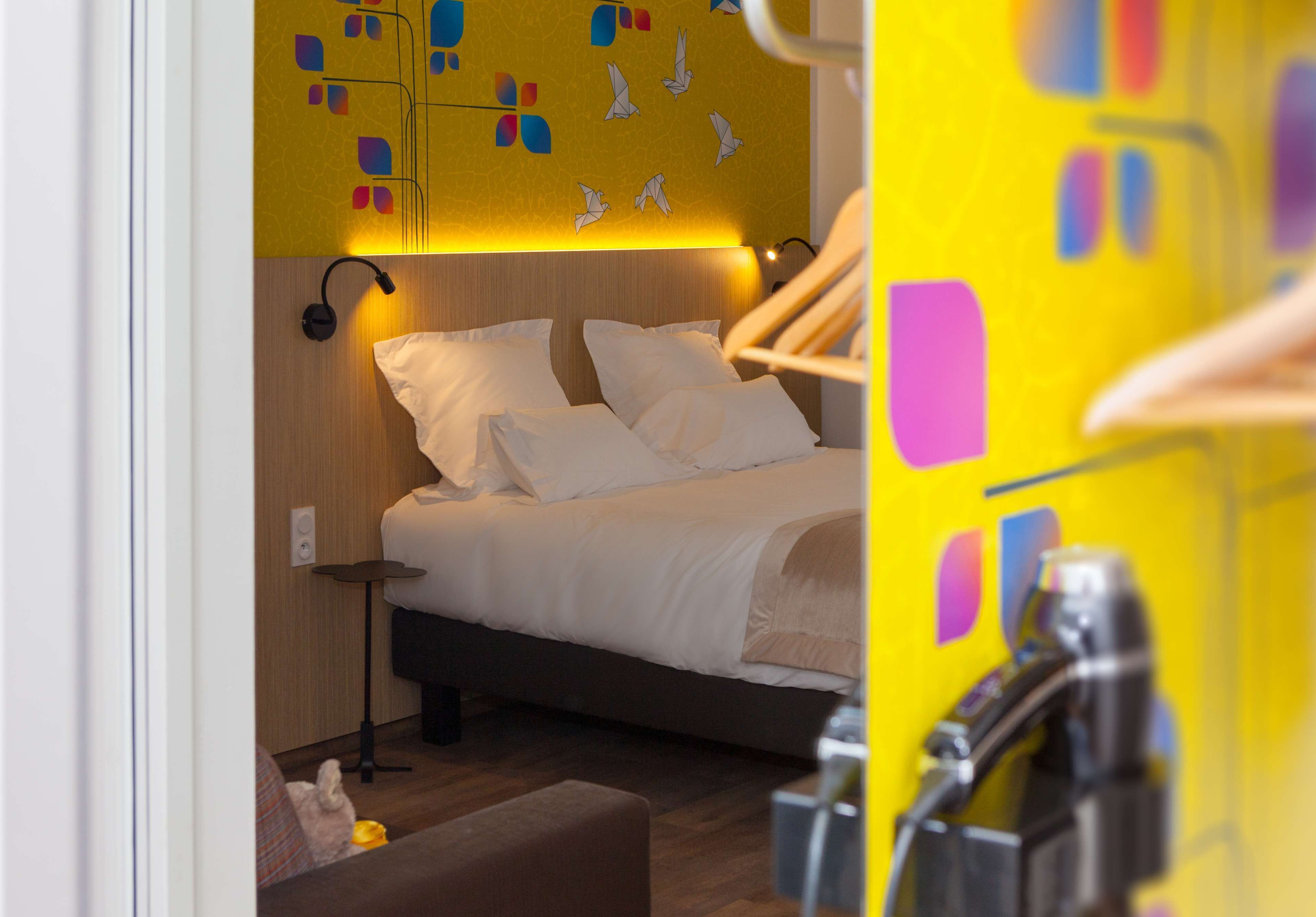 A modern hotel room with a neatly made bed, a bedside table, and a lamp.