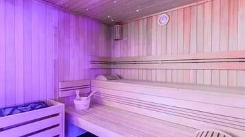 A sauna with wooden benches and a small table with a bucket and brush.