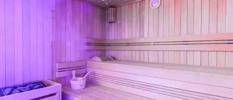 Una sauna con bancos de madera y una pequeña mesa con un cubo y escobilla.