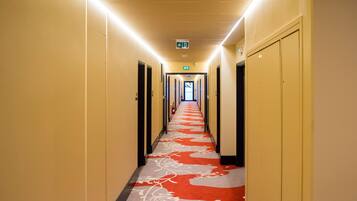 A hotel hallway with a red carpet, doors on both sides, and an exit sign at the end.