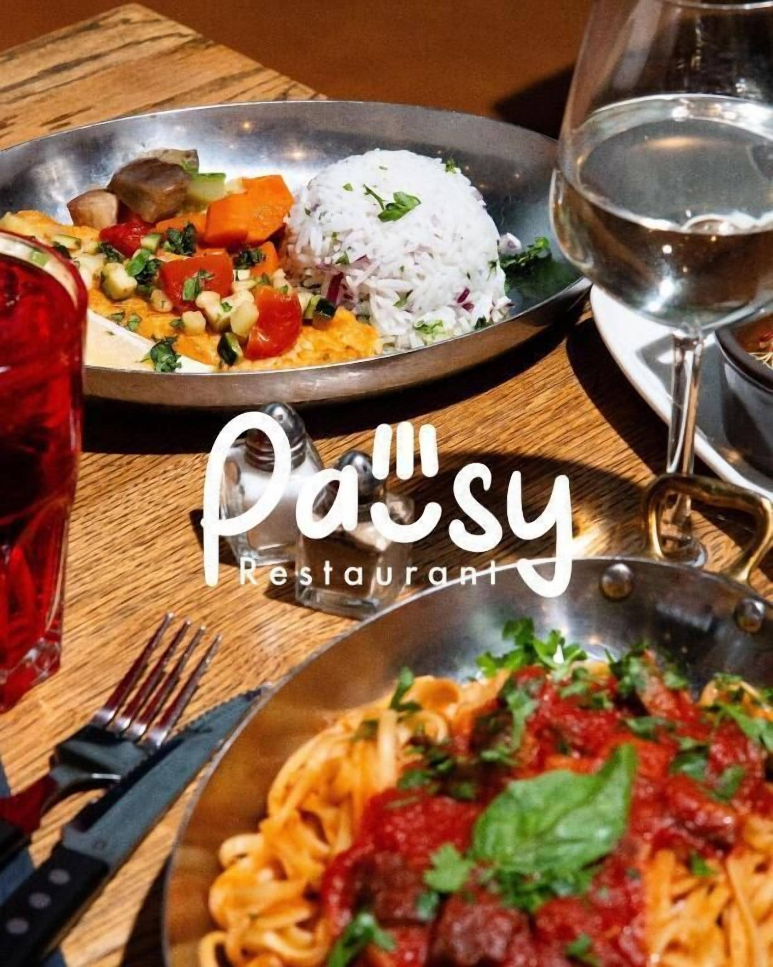 Eine Mahlzeit mit Reis, Gemüse und Pasta, dazu ein Glas Wasser auf einem Holztisch.