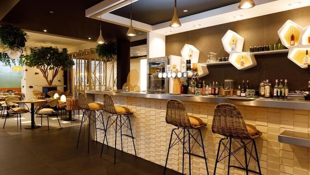 A modern bar area with wicker bar stools, a brick wall, and hexagonal light fixtures. - Kyriad Prestige Hôtel and Spa, Amiens Nord (Poulainville)