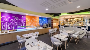 A modern restaurant with a colorful wall mural, white tables and chairs, and a bar area with hexagonal shelves. - Kyriad Prestige Hôtel and Spa, Amiens Nord (Poulainville)