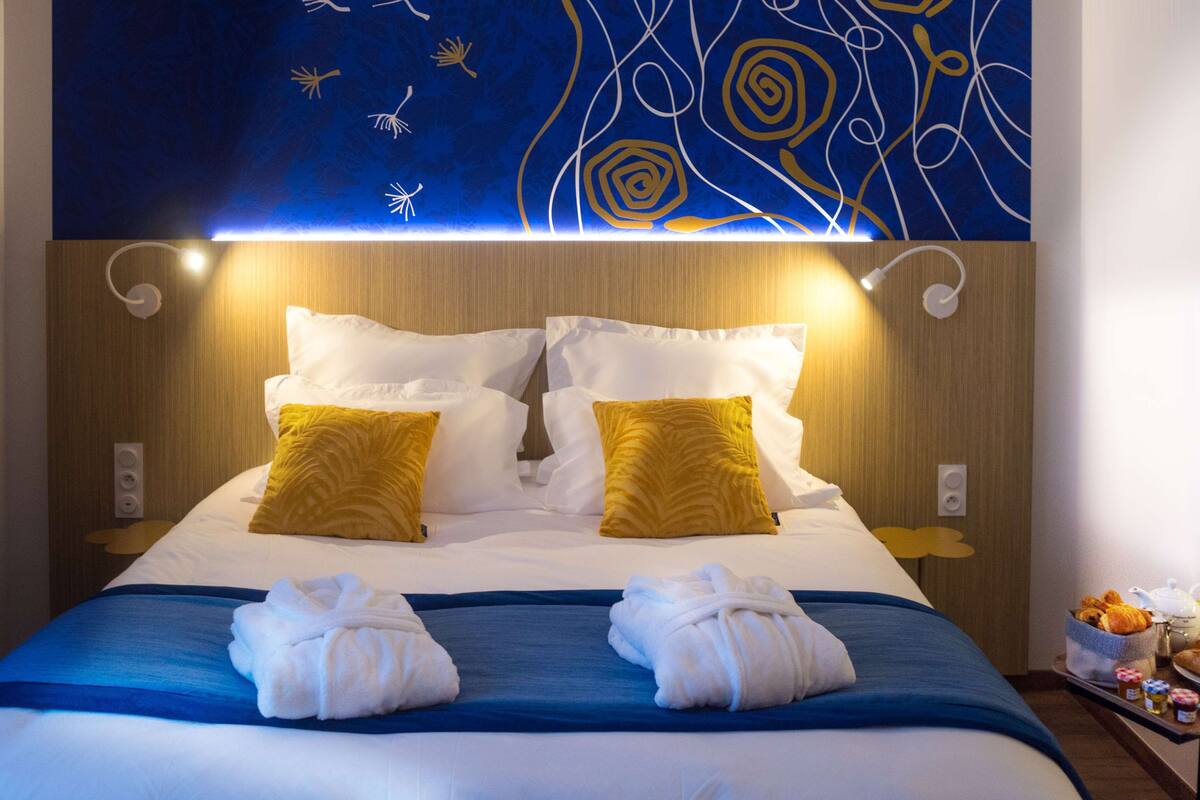 A hotel room with a neatly made bed, two pillows, and a tray with towels and breakfast items.