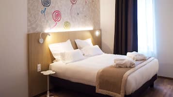 A neatly made bed with white linens and a beige throw blanket, a bedside table with a lamp, and a wall with abstract art.