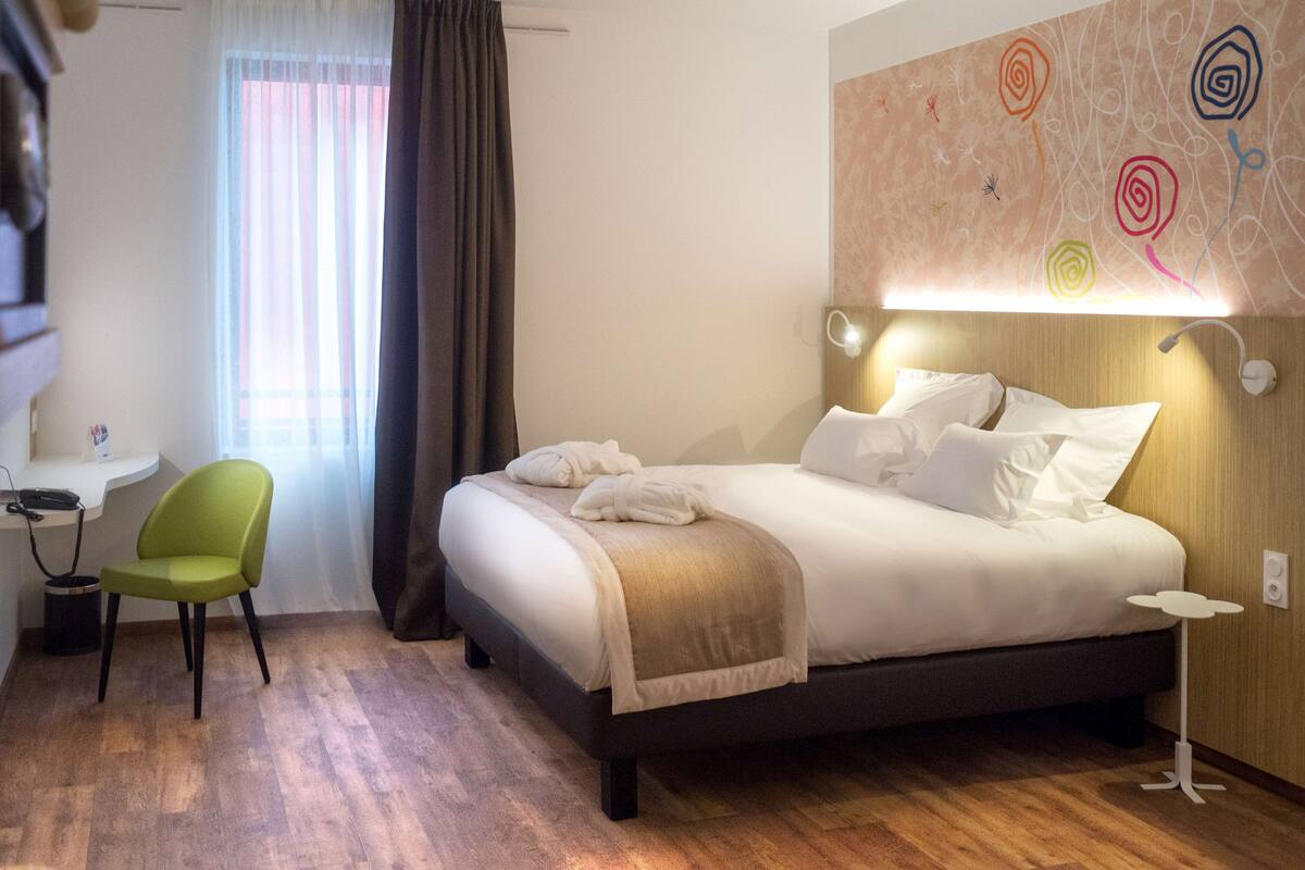 A hotel room with a bed, a desk, a chair, and a wall with abstract art.