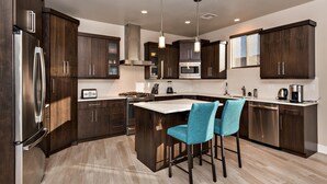 A modern kitchen with dark wood cabinets, stainless steel appliances, and a central island with bar stools. - Fish Rock Retreat Holiday home 3 (St. George)