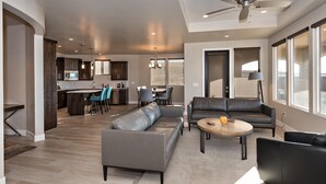 A spacious living area with a gray sofa, a coffee table, and a dining area with chairs and a kitchen in the background. - Fish Rock Retreat Holiday home 3 (St. George)