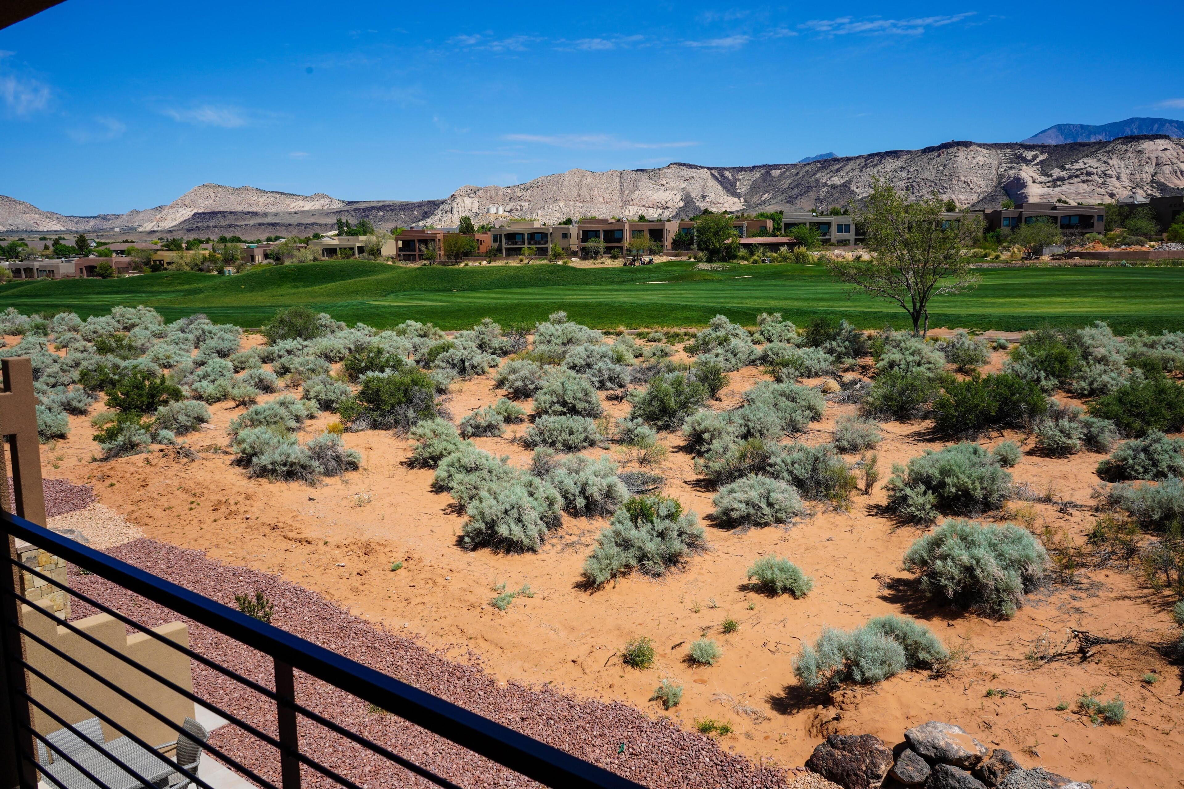 A desert landscape with sparse vegetation, a golf course, and a building complex in the background.