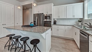 A modern kitchen with white cabinets, granite countertops, stainless steel appliances, and a central island with bar stools. - The Perfect Escape (St. George)