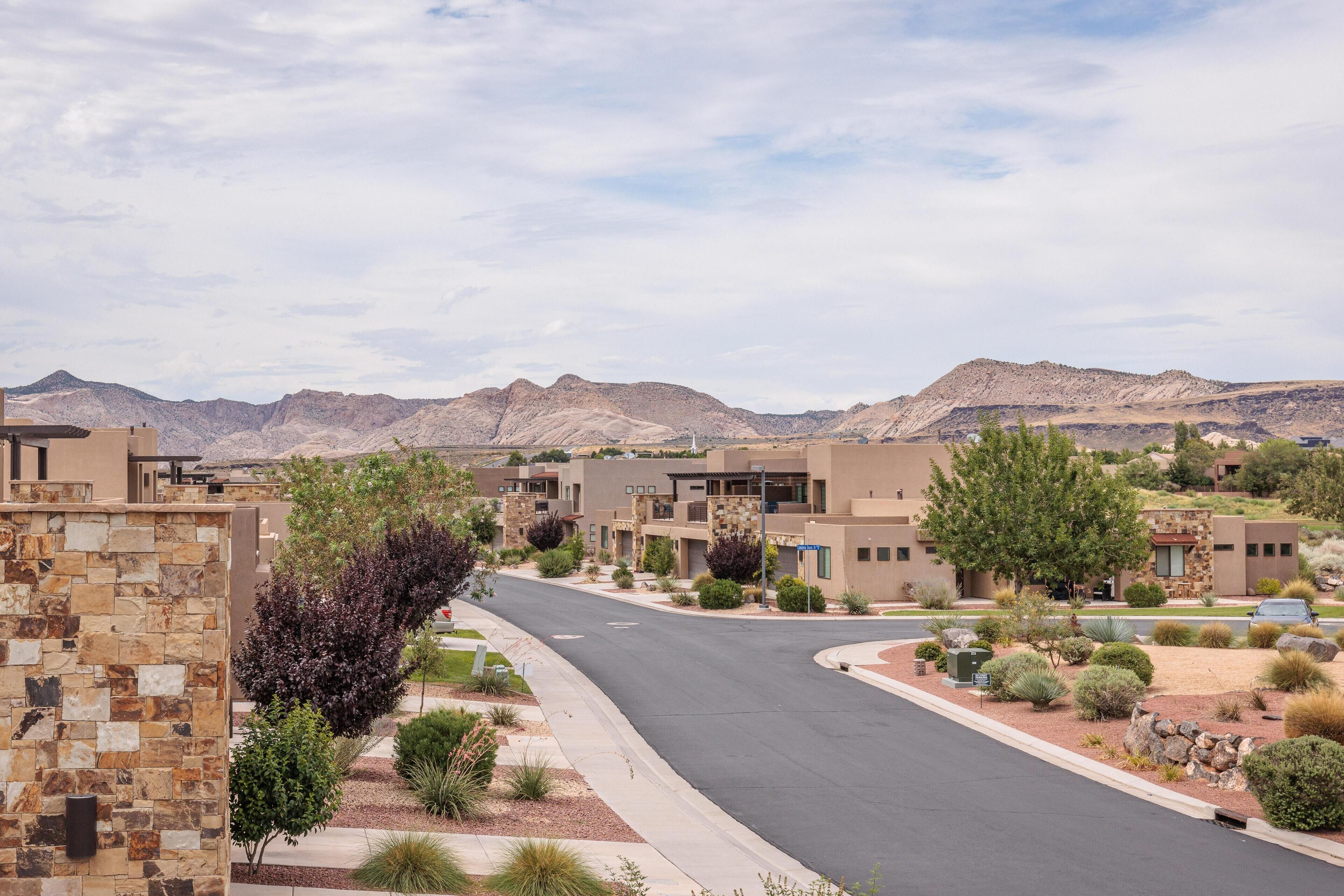 A residential street with modern houses, a stone wall, and a clear view of distant mountains.