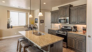 A kitchen with granite countertops, dark wooden cabinets, stainless steel appliances, and pendant lighting. - Suite Escapes (St. George)