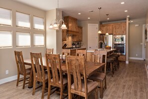 A spacious kitchen with wooden cabinets, a central island, and a dining area with wooden chairs. - I Could Live Here (St. George)